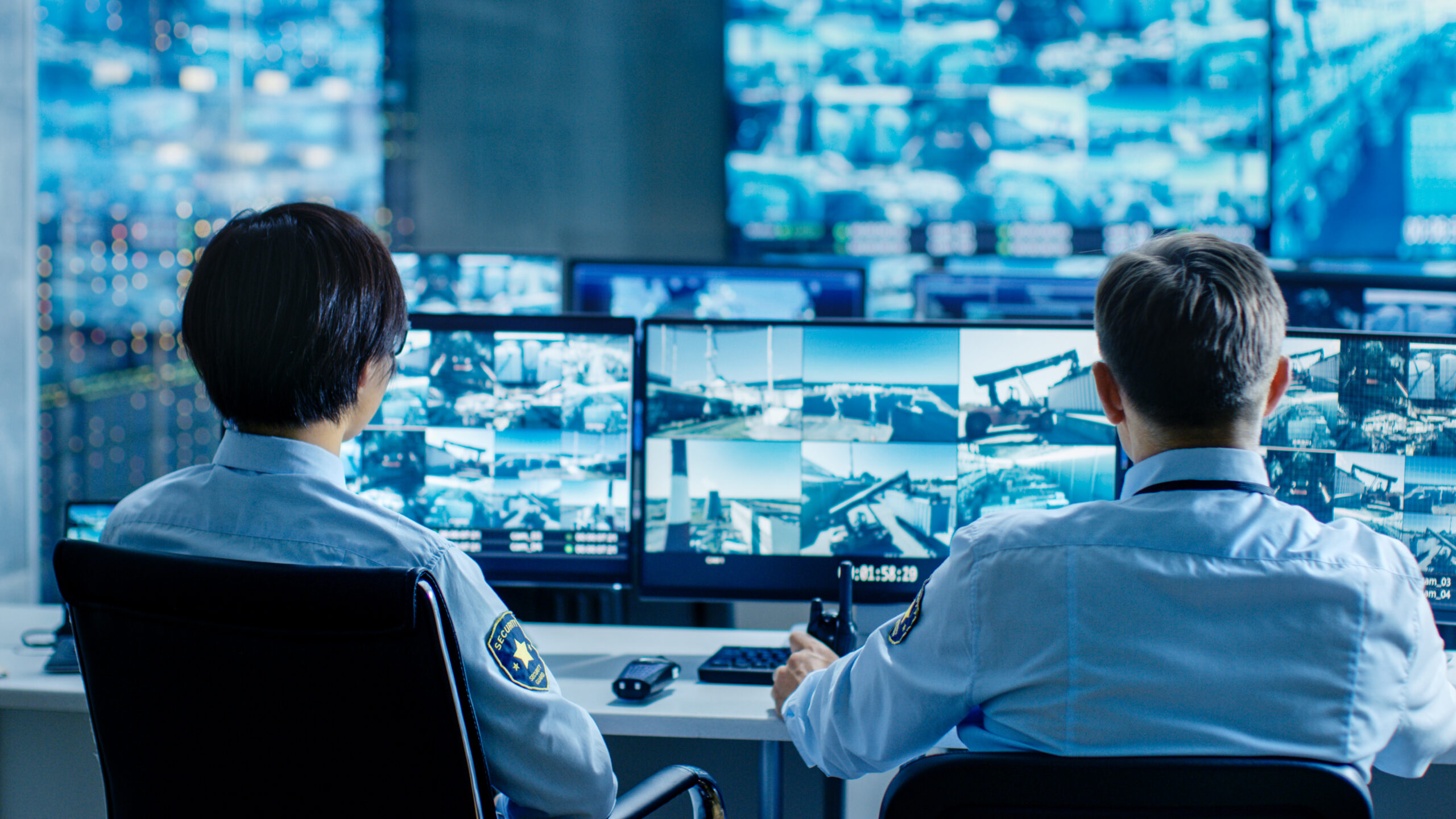 In the Security Control Room Two Officers Monitoring Multiple Screens for Suspicious Activities, They Report any Unauthorised Activities. They Guard Object of National Importance.