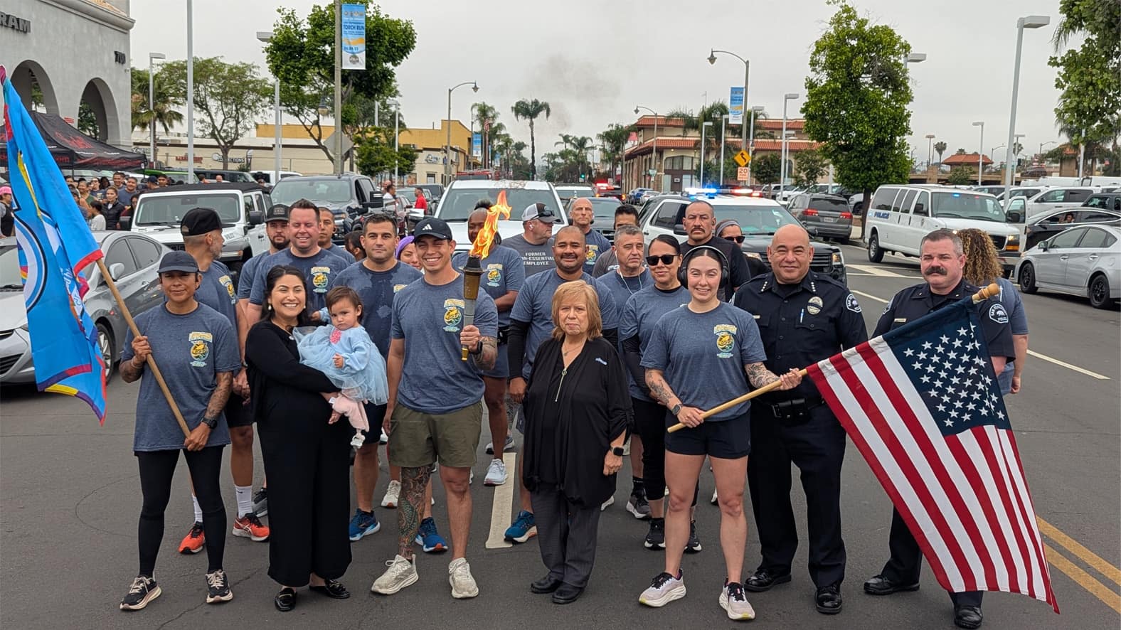 Group photo of San Fernando city officials, police officers, and community members standing together in front of the Rydell Dealership during the 2025 Law Enforcement Torch Run.