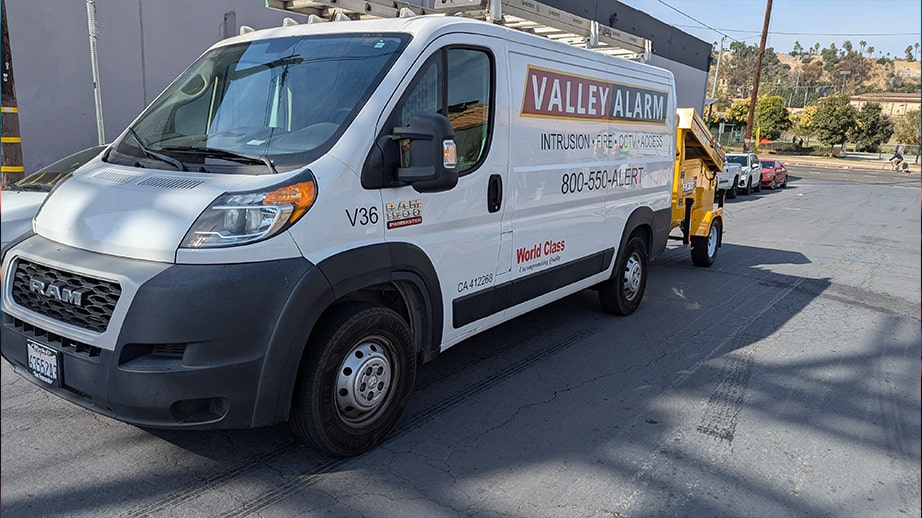 Valley Alarm service van towing a yellow mobile security trailer to a job site in Los Angeles