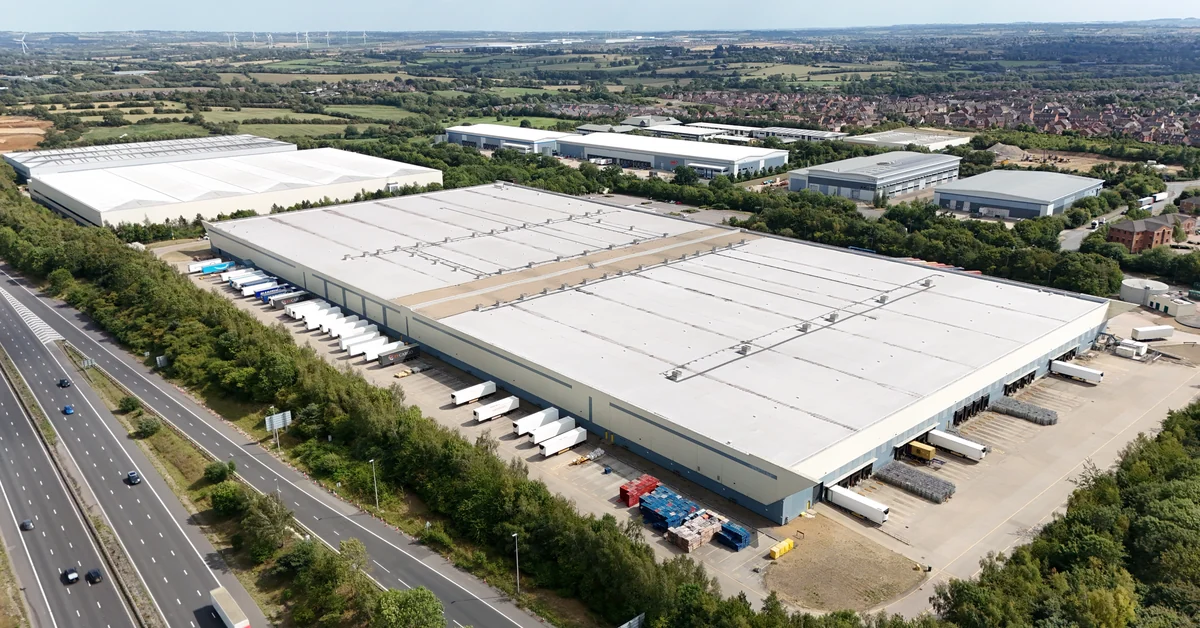 Aerial view of a distribution center with trailers backed into loading dock doors alongside a freeway
